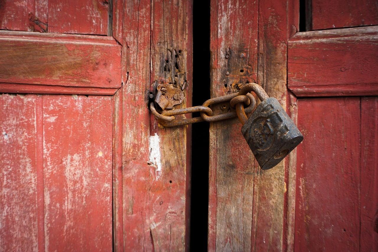 Image d'un cadenas et d'une chaîne fermant une porte abimée qui représente une protection contre les squatteurs