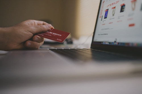 Photographie d'un consommateur tenant une carte de crédit devant un ordinateur illustrant ici les pratiques commerciales déloyales
